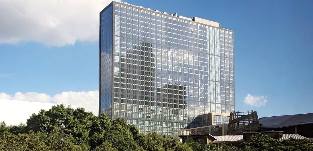 The glazed tower of Fairmont & Raffles Makati rising above the tree line in Manila, under a bright sky.